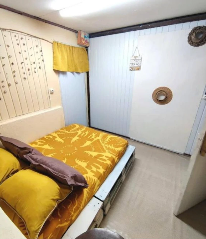 Une chambre double : grand lit sur palettes, draps jaunes, murs en lambris blanc