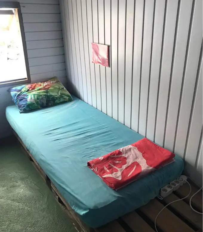 Un lit du dortoir, drap turquoise et serviette pliée, contre un mur en lambris blanc