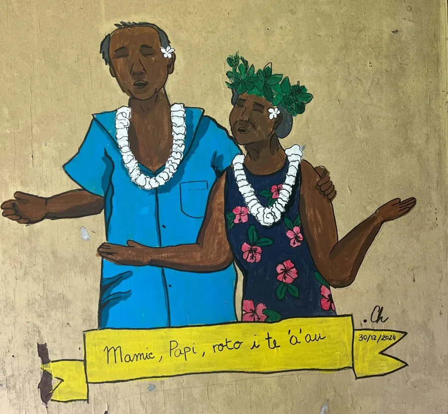 Fresque peinte sur un mur de l'auberge : Mamie en robe à fleurs et couronne de feuilles, Papi en chemise bleue, tous deux avec un collier de fleurs blanches, au-dessus d'une banderole jaune « Mamie, Papi, roto i te 'a'au »